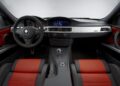 Interior view of a BMW E90 M3 collector car featuring a black and red leather interior, manual gear shift, steering wheel, and central touchscreen display.