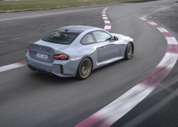 A grey BMW coupe from BMW USA drives on a racetrack, captured from behind as it rounds a corner—exemplifying the dynamic spirit fueling BMW’s sales growth in H1 2025.