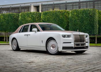 A one-off white and brown Rolls-Royce Phantom Dentelle sedan is parked on a cobblestone driveway in front of trimmed hedges and a modern building.