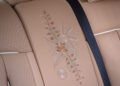 Tan leather car seat with detailed floral embroidery, inspired by the Phantom Dentelle, and a black seatbelt across it—a true one-off Rolls-Royce interior masterpiece.