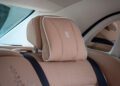 Luxury car rear seat with beige leather upholstery, embroidered detailing, a headrest featuring the Rolls-Royce logo, and visible seat belts—an exquisite detail from the one-off Phantom Dentelle.