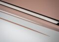 Close-up of the edge of a closed, slim, rose gold laptop on a white surface with a matching accent line, reminiscent of the refined elegance found in the Phantom Dentelle one-off by Rolls-Royce.