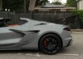 Side view of a gray 2025 Chevrolet Corvette ZR1 with black rims, rear spoiler, and ZR1 badge, parked on a street in front of a fence and houses. This 064HP powerhouse is now for sale.