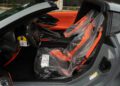 The interior of a 2025 Chevrolet Corvette ZR1 sports car with gray and orange accents, featuring plastic covers on the seats and steering wheel, viewed from the driver's side door.