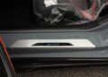 Close-up of a 2025 Chevrolet Corvette ZR1 door sill with a metallic "ZR1" badge, gray body paint, and part of a seat covered in protective plastic visible—perfect for those seeking a Corvette ZR1 for sale.