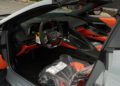 Interior view of a 2025 Chevrolet Corvette ZR1 for sale, showcasing black and orange seats with plastic covering on the passenger seat, plus visible dashboard and steering wheel controls—an impressive 1,064HP powerhouse.