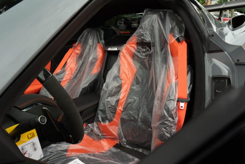 The interior of a 2025 Chevrolet Corvette ZR1 features orange and black seats covered in clear plastic protective covers, ready for sale.