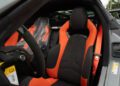 Close-up view of the 2025 Chevrolet Corvette ZR1 interior, showcasing a black and orange bucket seat, steering wheel, seatbelt, and dashboard details—befitting its impressive 1064HP performance.