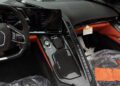 Interior of a 2025 Chevrolet Corvette ZR1 for sale, featuring a digital display, carbon fiber center console, black and orange trim, and protective plastic covering on the passenger seat.