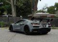A gray 2025 Chevrolet Corvette ZR1 is parked on a paved lot, viewed from the rear side, showcasing black wheels and a black rear spoiler. This powerful sports car with 064HP is for sale.