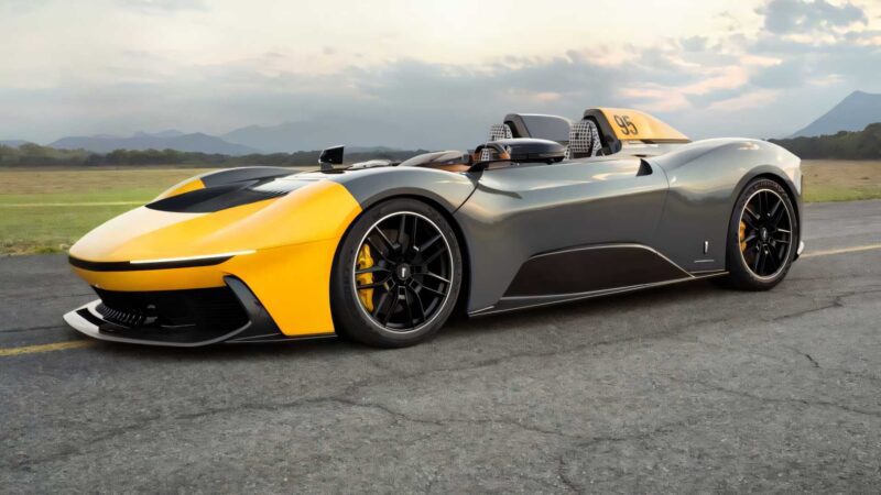 A sleek, yellow and gray two-seat sports car with an open cockpit—one of the most powerful production cars of 2025—is parked on an outdoor road, with mountains and a cloudy sky in the background.