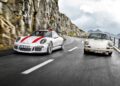 A modern 2016 Porsche 911 R and a classic white Porsche drive side by side on a winding mountain road, framed by rocky cliffs and cloudy skies.