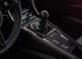 Close-up view of a 2016 Porsche 911 R’s center console featuring a manual gear shift, control buttons, and part of the steering wheel with a visible Porsche logo.
