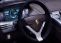 Close-up view of a Porsche car interior, highlighting the steering wheel with the Porsche logo, digital instrument cluster, and part of the center console—an elegant nod to the Carrera GT featured in the Tribute Capsule Collection.