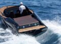 A person drives a modern, black Porsche Macan EV-powered Frauscher Fantom 850 with wooden deck detailing through blue ocean waves, setting a speed record in Monaco.