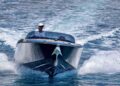 A man wearing sunglasses and a cap drives a black Porsche Macan EV-powered Frauscher Fantom 850 at high speed, creating waves as it sets a speed record in Monaco.