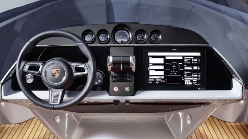 Close-up view of a yacht control dashboard with a Porsche steering wheel, analog gauges, digital displays, and controls—similar to the high-tech cockpit found in the Porsche Macan EV-Powered Frauscher Fantom 850 that set a speed record in Monaco.