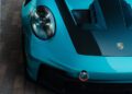 Close-up of the front left side of a Porsche Exchange 911 GT3 RS in PTS Ipanema Blue, featuring a carbon fiber hood, visible headlight, and tow hook.