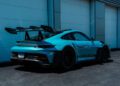 A PTS Ipanema Blue 911 GT3 RS with a large rear wing is parked in front of a row of white garage doors on a sunny day, showcasing the exclusivity found at the Porsche Exchange.
