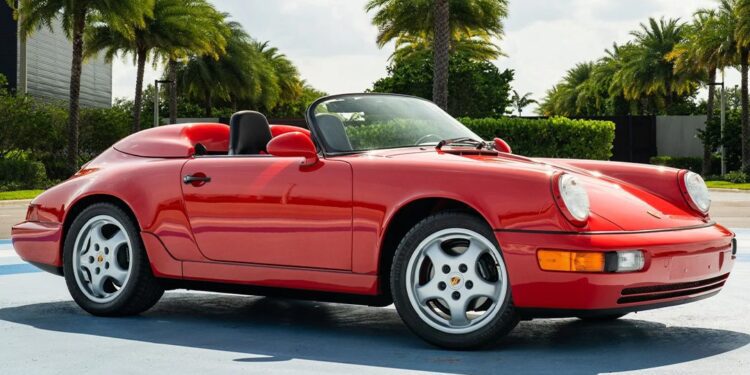 A red convertible sports car with the top down is parked outdoors on a sunny day, surrounded by palm trees—a stunning example of low mileage classic cars.