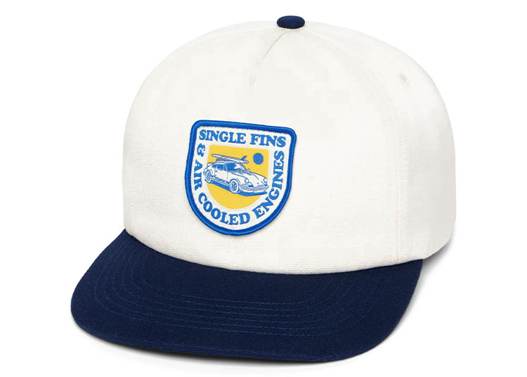 White baseball cap with a navy blue brim and a patch on the front reading "Single Fins & Air Cooled Engines," featuring an illustration of a Porsche with a surfboard—crafted in collaboration with Almond Surfboards.