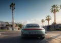 A Porsche 911 is shown from the rear driving on a suburban street lined with palm trees and modern houses under a partly cloudy sky.