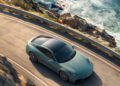 A silver sports car drives along a coastal road with cliffs and waves crashing on rocks below.