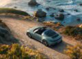 A green Porsche convertible, one of the striking new 911 variants, is parked on a dirt road overlooking a rocky coastline with waves and seaside cliffs at sunset.
