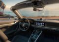 Interior view of a new 911 convertible sports car parked near a coastal road, showcasing the dashboard, steering wheel, and an ocean view with palm trees through the windshield—exemplifying the allure of Porsche 911 variants.