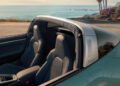 A Porsche 911 convertible with two leather seats is parked by a coastal road, with palm trees and the ocean visible in the background.
