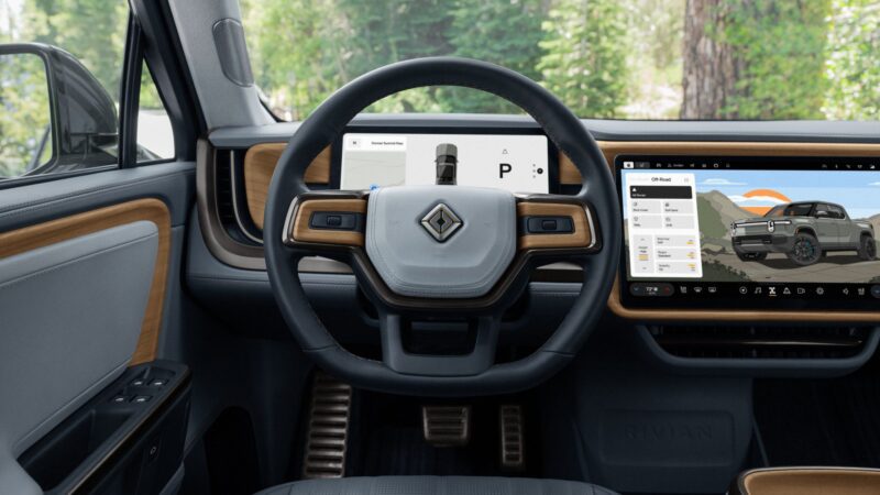 The interior of a Rivian Gen 2 vehicle showing a steering wheel, digital dashboard display, and touchscreen center console with navigation and controls.
