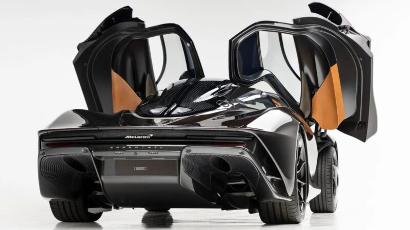 Rear view of an ultra-low mile McLaren Speedtail with both butterfly doors open, showcasing its sleek design, exposed carbon fiber elements, and $250k in MSO options—this stunning car is heading to auction.