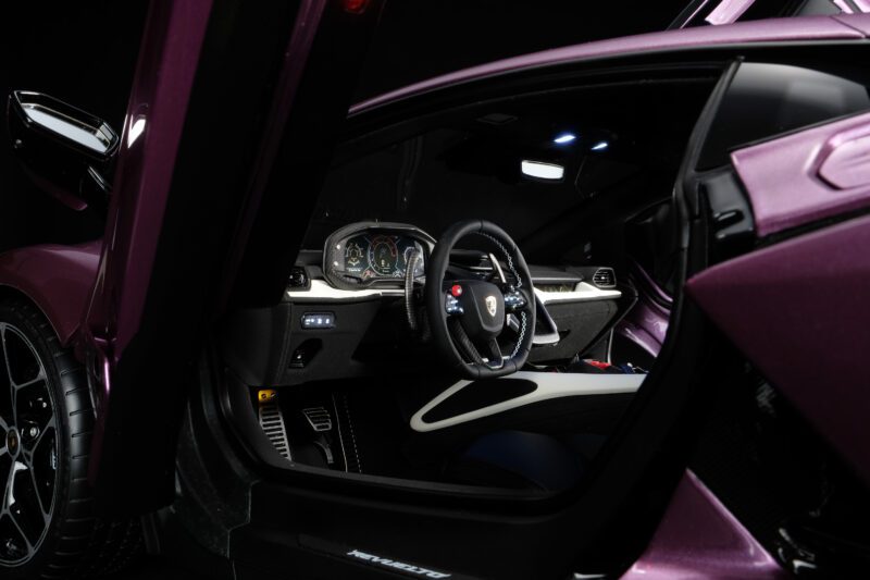 Close-up of the driver's side interior of a purple 1:8 Revuelto model with the door open, showcasing the steering wheel, dashboard, and pedal area—a standout piece for any Amalgam Lamborghini collection.