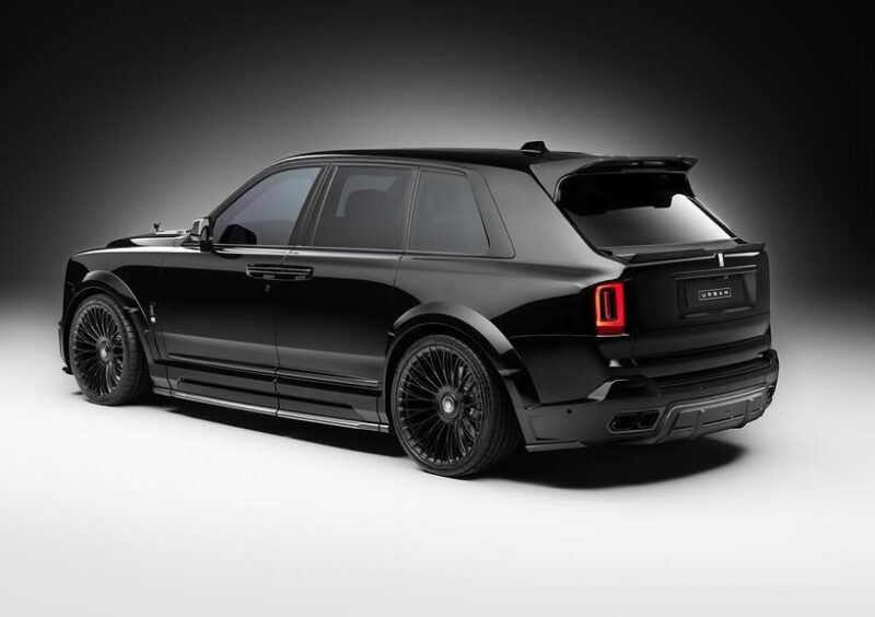 A black Rolls-Royce Cullinan with tinted windows and custom 24-inch rims is parked in a studio with a plain gradient background.
