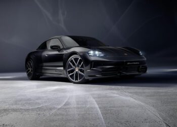 A 2026 Taycan Black Edition Porsche sports car is parked on a smooth, light-gray surface with a dark, gradient background.