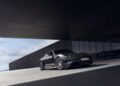 A sleek 2026 Taycan Black Edition sports car is parked in front of a modern glass building under an overhanging structure on a sunny day.