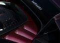 Close-up of a Ferrari SF90 XX Spider engine cover with striking red carbon fiber detailing and the Ferrari logo visible, captured at Ferrari Beverly Hills on a shiny black surface.