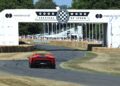 A red Ferrari F80 speeds along the track at the Goodwood Festival of Speed, passing under an event banner as crowds watch the thrilling Amalfi Reveal unfold in the background.