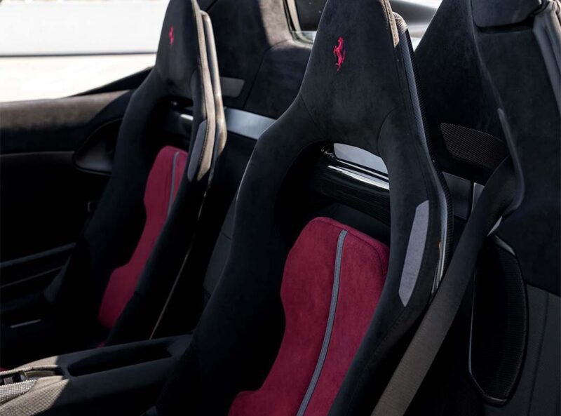Two black sport seats with red inserts and a Ferrari logo on the headrests inside a SF90 XX Spider, featuring exquisite details inspired by Ferrari Beverly Hills.