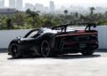 A black SF90 XX Spider with a large rear spoiler is parked on a rooftop, overlooking the city skyline and palm trees, showcasing its Red Carbon Fiber accents.