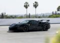 A black Ferrari SF90 XX Spider is parked outdoors on a sunny day, featuring Red Carbon Fiber accents, with palm trees and distant hills in the background—a perfect scene from Ferrari Beverly Hills.