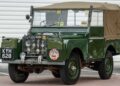 A vintage green Land Rover Classic with a canvas top, rally stickers, and license plate KYH 628 sits parked on brick and asphalt—the perfect nod to the icons set to showcase at the 2025 Pebble Beach Concours d'Elegance.