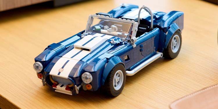 A blue and white LEGO Shelby Cobra 427 model car, resembling a classic sports convertible, sits on a light wooden table—a striking build set for car enthusiasts and collectors.