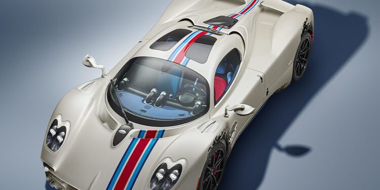 A white sports car with blue and red racing stripes, two seats, and aerodynamic design, photographed from above on a neutral background.