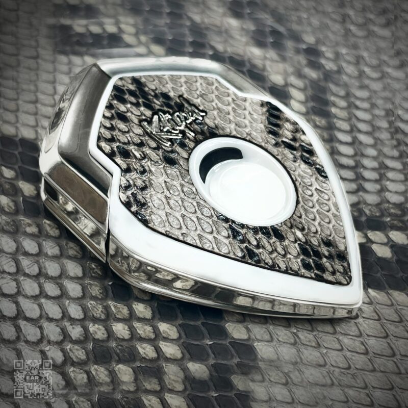 A luxury Bugatti car key with a snakeskin pattern and metallic edges placed on a matching snakeskin surface—an essential style upgrade for those seeking luxury accessories.