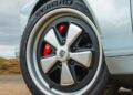 Close-up of a car's front wheel featuring a silver Porsche rim, red Brembo brake caliper, and a Michelin tire—evoking the spirit of an air-cooled 911 restored by Theon Design on a paved road.