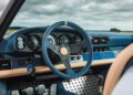 Close-up of a vintage car’s blue and beige interior, showcasing the steering wheel, dashboard gauges, gear shift, and metallic pedals—a refined look inspired by Theon Design’s Air-Cooled 911 approach to power-to-weight excellence.