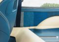 Close-up of a car’s blue and cream leather interior with a blue checkered panel, seatbelt, window, and trees visible outside—crafted by Theon Design for their signature Air-Cooled 911.