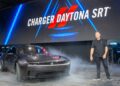 A man stands next to a Dodge Charger Daytona SRT car on a stage with smoke, under a large display reading "Charger Daytona SRT," as Stellantis gets Back in the Driver’s Seat: Tim Kuniskis to Lead Stellantis’ Comeback In North America.