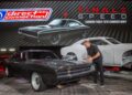 A man stands next to a black 1970 Dodge Charger, featuring a white carbon fiber Charger body and large promotional graphics in the background—Back in the Driver’s Seat: Tim Kuniskis to Lead Stellantis’ Comeback In North America.